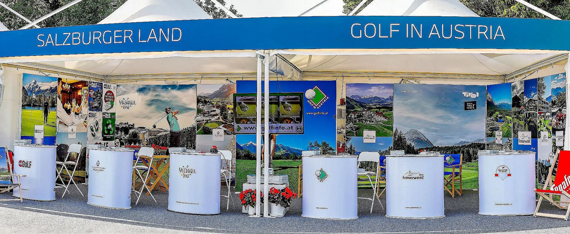 Werbestand mit blauen und weißen Elementen, die für Golf in Österreich werben. Es gibt Schilder mit Landschaftsbildern und Tische für Informationsmaterial.