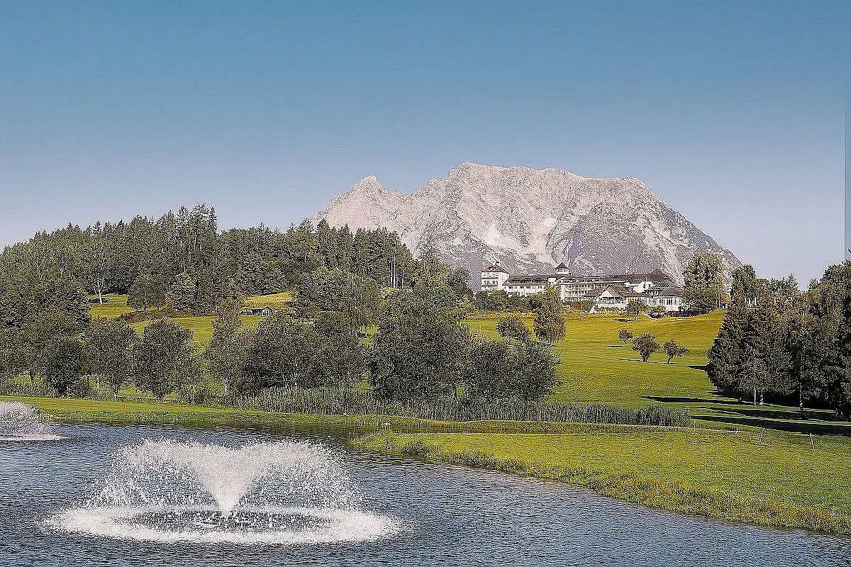Malere Landschaft mit einem See im Vordergrund, umgeben von Bäumen, mit einem großen Berg im Hintergrund und blauen Himmel darüber.