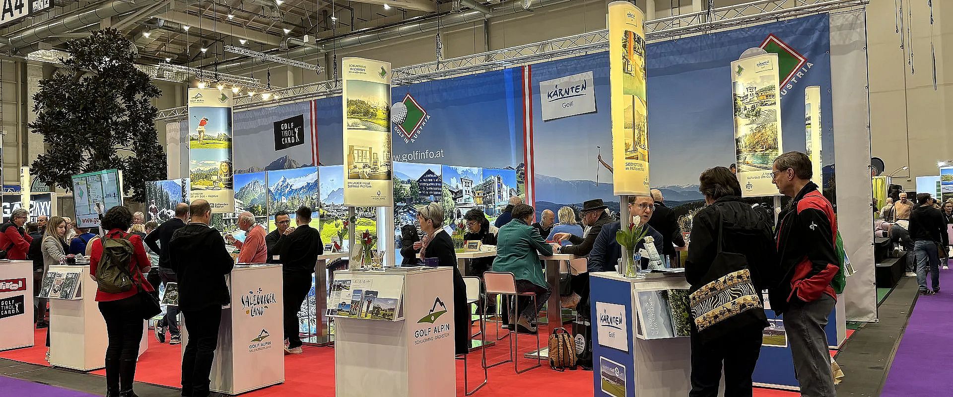 Menschen an bunten Messeständen in einer großen Halle, mit dekorativen Bannern und Prospekten über Freizeitaktivitäten in einer Tourismusregion.