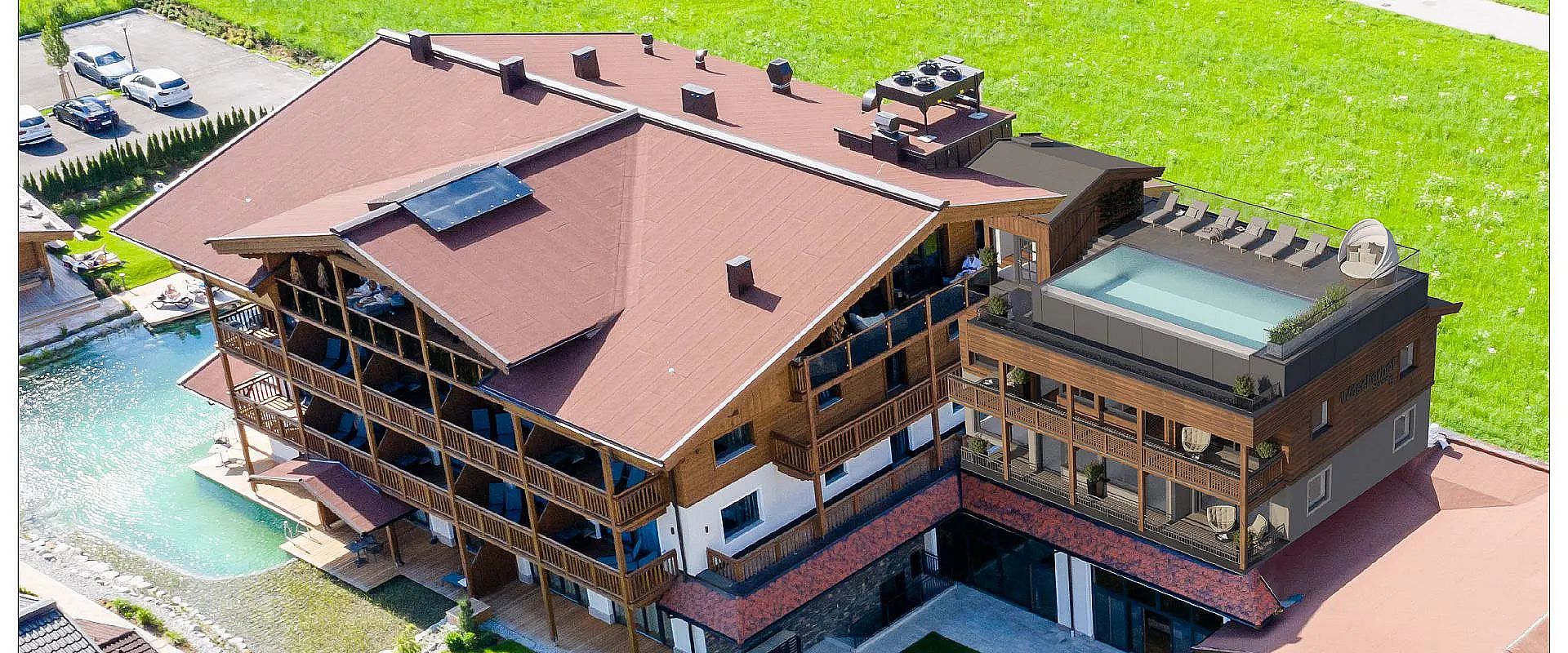 Eine Luftaufnahme eines großen, modernen Holzgebäudes mit braunen Dächern, Balkonen und einem Dachgarten. Das Gebäude steht auf einem grünen Rasen.