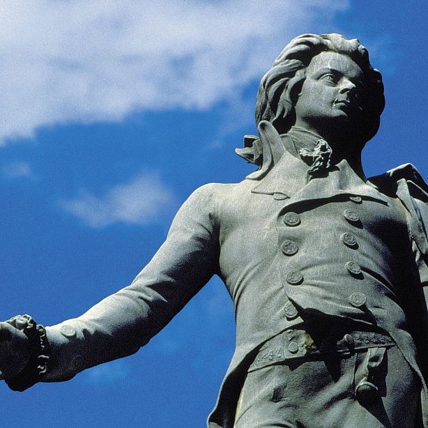 A close-up of a historical statue with a blue sky in the background, showcasing detailed craftsmanship and a strong, dignified pose.