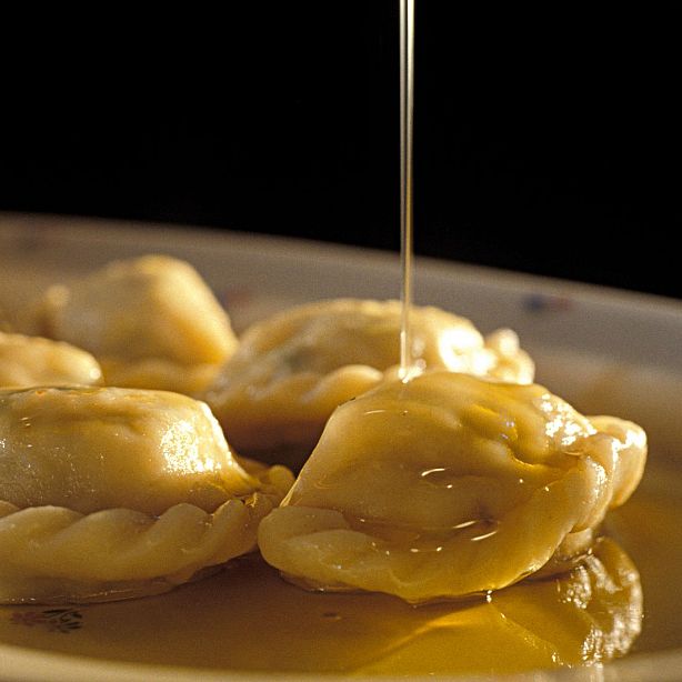 Close-up of dumplings on a plate being drizzled with honey, highlighting their shiny, golden appearance against a blurred background.