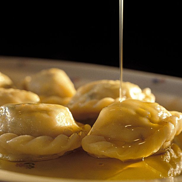 Close-up of dumplings being drizzled with sauce on a plate, creating a shiny gloss. The dumplings appear golden brown and are neatly arranged.