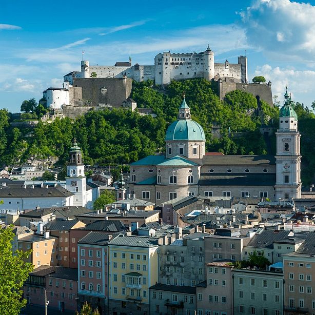 Cityscape with a fortress on a hill, historic buildings, and a large dome under a clear blue sky.