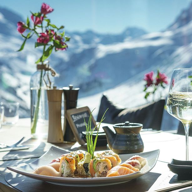Outdoor dining setup with gourmet food, a wine glass, flowers, and scenic mountain background, evoking a sense of luxury and tranquility.