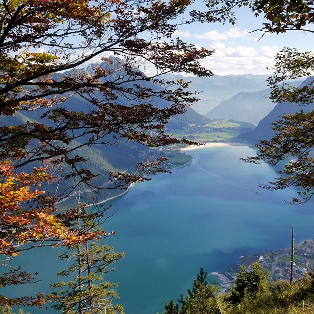 A tranquil lake surrounded by mountains and autumn trees, under a partially cloudy sky, creating a picturesque landscape.