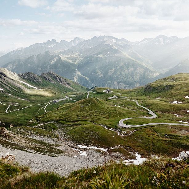 A scenic view of winding roads through lush green mountains under a cloudy sky with visible distant peaks.