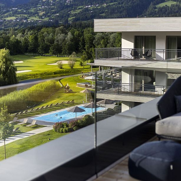 View from a balcony of a resort with a pool, golf course, and lush greenery, providing a serene and luxurious ambiance.