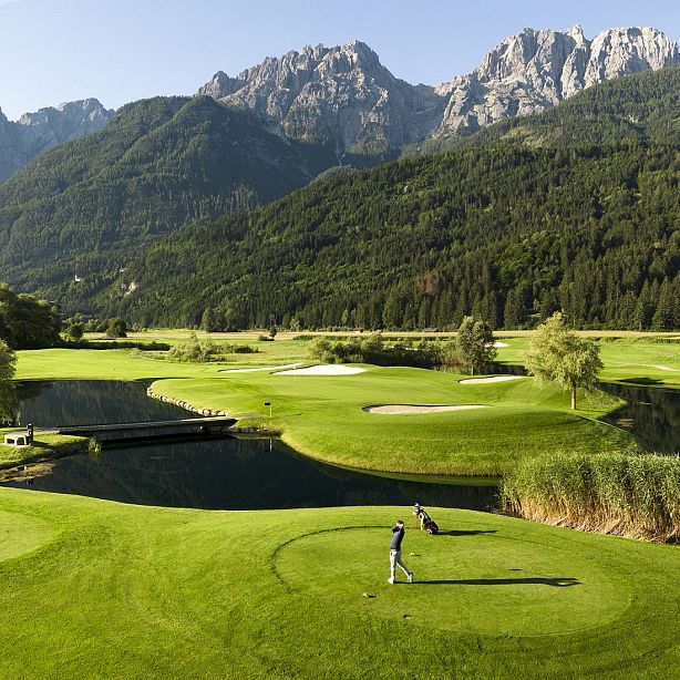 Golf course with a mountainous backdrop, lush green fairways, and a serene landscape under a clear sky.
