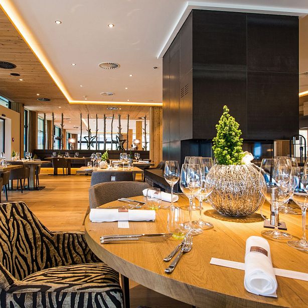 Elegantes Restaurant mit stilvoll gedeckten Tischen, modernen Holzelementen, schicker Beleuchtung und großzügigen Fenstern für viel Tageslicht.