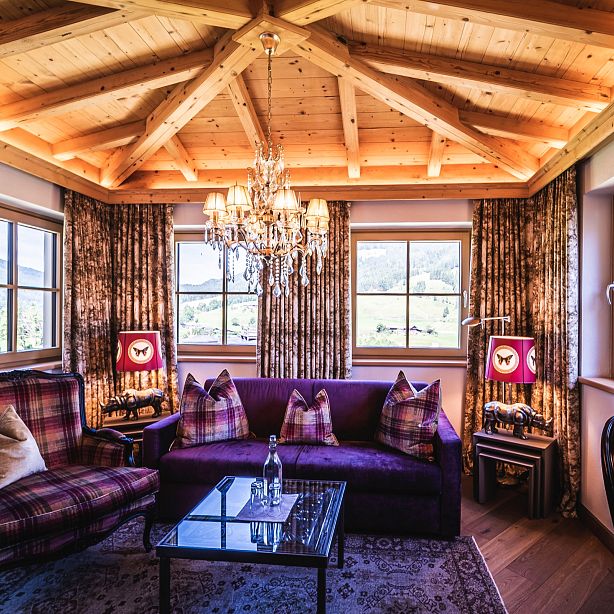 Rustic living room with wood ceiling, plaid furniture, chandelier, large windows, wooden beams, and a warm, inviting atmosphere in a countryside setting.