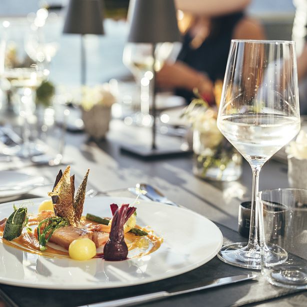 A gourmet dish on a white plate with artistic presentation, surrounded by elegant tableware on a restaurant table setting.