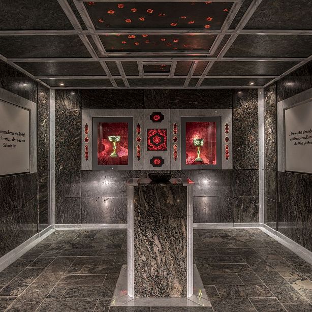 A dimly lit room with red glowing alcove, featuring geometric patterns, symbols, and two chalices, creating a mystical and ceremonial atmosphere.