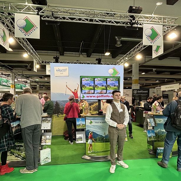 People at a golf exhibition booth with banners, screens, and promotional materials, showcasing golf-related services and products.