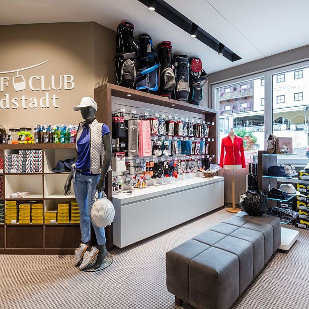 Ein Golfgeschäft mit Regalen voller bunter Golfbälle, Bekleidung und Ausrüstung. Eine Schaufensterpuppe trägt golftypische Kleidung. Helle und moderne Einrichtung.