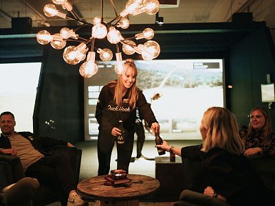 A cozy room with friends sitting around a table, enjoying drinks and conversation under a stylish chandelier with exposed bulbs, creating a warm atmosphere.