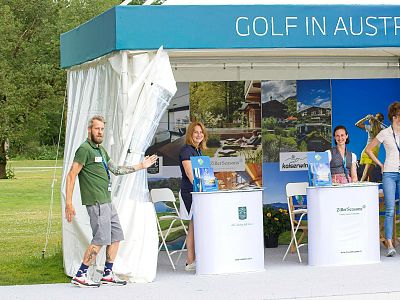 Outdoor event booth promoting golf in Austria with people and scenic backdrops.