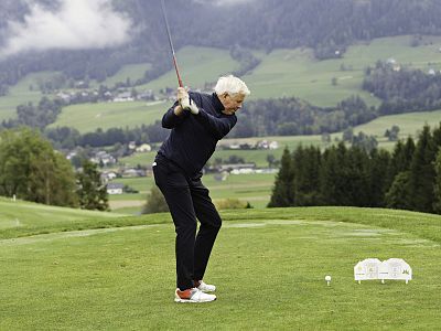 A golfer swings on a scenic course with green hills and cloudy sky in the background, highlighting the peaceful nature of the game.
