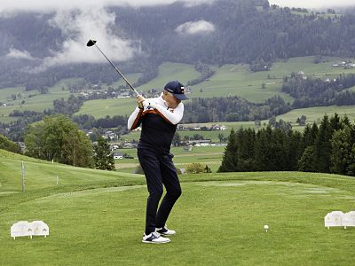 Golfer taking a swing on a verdant golf course with mountains and cloudy sky in the background, creating a tranquil and scenic view.
