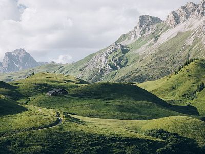 Green hills and towering mountains under a cloudy sky create a serene and picturesque landscape, perfect for nature and photography enthusiasts.