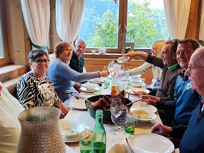 A group dining in a cozy chalet, with sunlight through large windows, wooden interior, and picturesque views in the background.