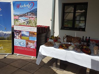 An outdoor event setup with a table of food, drinks, and promotional banners under a sunny sky, suggesting a festive and inviting atmosphere.
