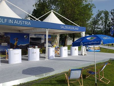 Outdoor golf exhibit in Austria with tents, banners, and seating focused on promoting the Salzburg region.