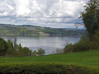 View of a tranquil lake with surrounding greenery and a cloudy sky.