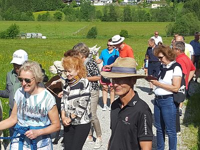 A group of tourists walking along a country path, guided by a woman with a donkey. They are in sunny weather, surrounded by green fields and distant houses.