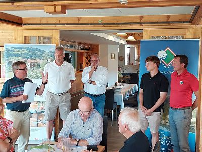 Group of people in a restaurant during a presentation. Some are standing, discussing, while others are seated. Banners are visible in the background.