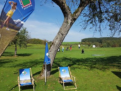 A grassy field with banners, deck chairs, and people in the background under a clear blue sky.