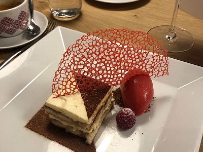 Layered cake with raspberry sorbet, red sugar garnish, and a raspberry on a white plate in a restaurant setting.