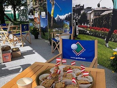 Outdoor setting with golf posters, deck chairs, and a table with pastries decorated with Austrian flags.