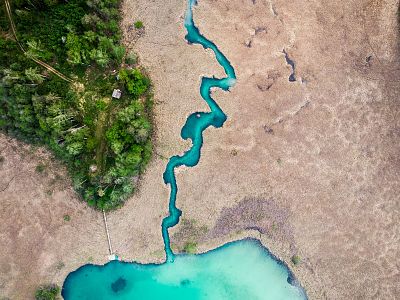 Aerial view of a bright turquoise river winding through a contrasting landscape of green vegetation and dry brown terrain.