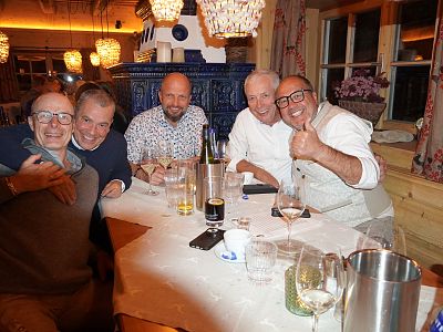 Five men sitting at a restaurant table smiling, with warm lighting and decorative lamps around them, creating a cozy atmosphere.