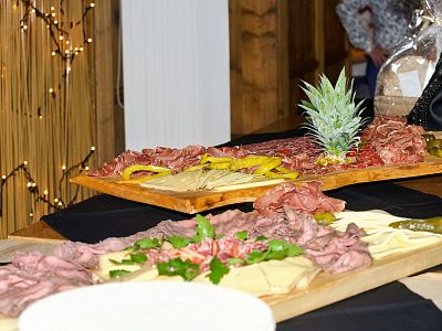 Wooden boards with assorted cured meats, cheeses, and garnishes, including a pineapple centerpiece, set on a table with decorative lights.