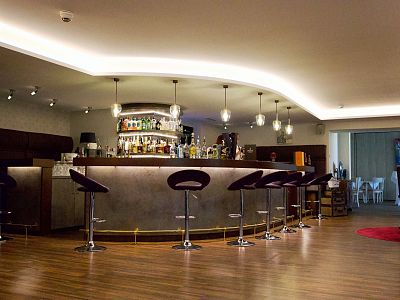 A modern bar with a curved counter, high stools, and contemporary lighting. Bottles are lined up behind the counter in an elegant setting.