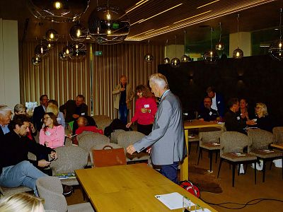 People in a modern room with contemporary lighting, engaged in conversation and seated around tables, creating a lively and welcoming environment.