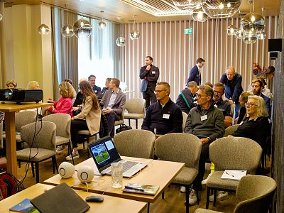 People seated in a modern conference room attending a workshop, facing a presentation screen. The room has stylish lighting and a professional yet relaxed ambiance.
