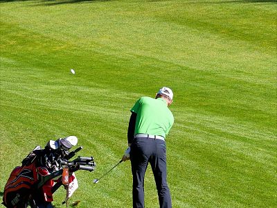 A golfer in a green shirt concentrates on making a shot on a lush green golf course, with a red golf bag nearby.