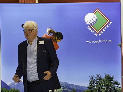 Man in front of a promotional backdrop for Golf in Austria, showing a golfer and mountains. He is dressed in a suit, suggesting a formal event.