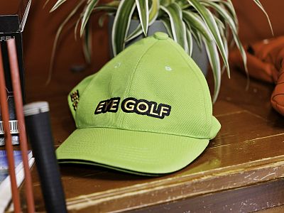 A green cap with 'EYE GOLF' text on a wooden surface, near a leafy plant and other items, creating a sporty and casual ambience.