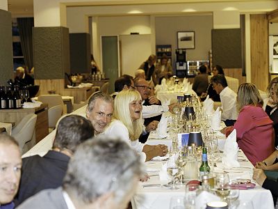 A long dining table set for a formal dinner with people engaged in conversation, wine glasses, and elegant table settings in a warm, inviting atmosphere.