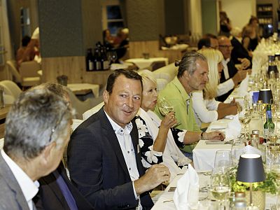 Eine Gruppe von Menschen sitzt an einem langen, festlich gedeckten Tisch in einem Restaurant. Sie lachen und genießen Getränke in einer gemütlichen Atmosphäre.