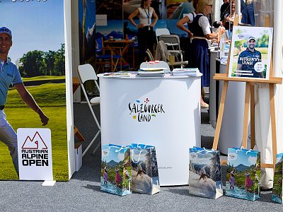 A promotional booth with outdoor activity theme, featuring colorful bags, banners, and a countertop with brochures at an event.