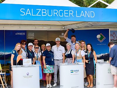 A group of people at a Salzburger Land booth, wearing traditional attire and branded clothing, smiling at an outdoor event.