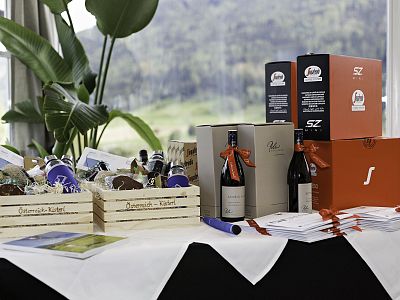 A table with assorted gift baskets and wine boxes, decorated with ribbons, set in front of a scenic window view.