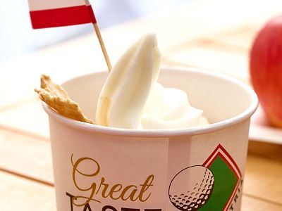 Cup of frozen yogurt with a red flag and biscuit, placed on light wood table. Cup features a golf theme design.