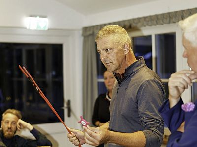 Man with red pointer leads discussion in a room with large windows. Others sit and listen, contributing to an engaging conversation.