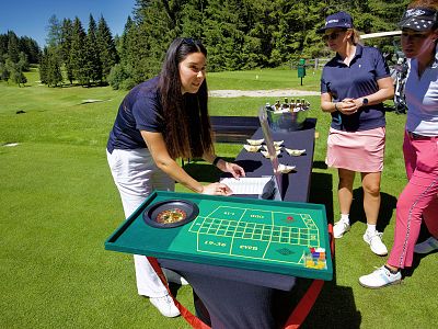 People gathered around a casino table on a grassy field, participating in an outdoor event with trees in the background.